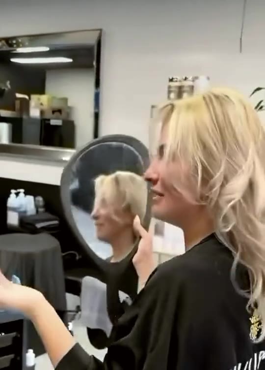 A Building Beauty client smiling at her new blonde hair in a hand mirror